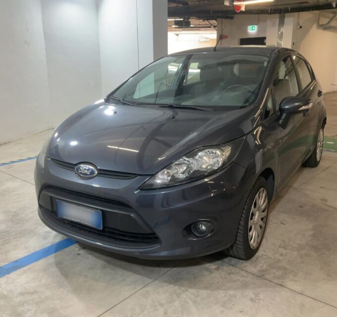 Gray Ford sedan parked in an indoor parking garage, front-left view showing headlights and grille.