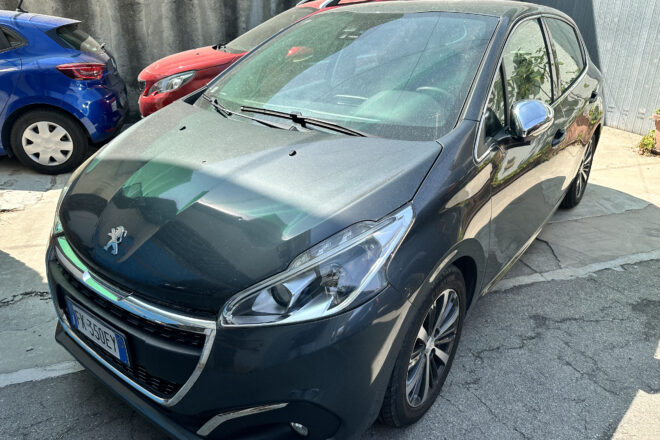 Front-left view of a dark gray Peugeot car parked in a lot beside a blue car and a red car behind it.