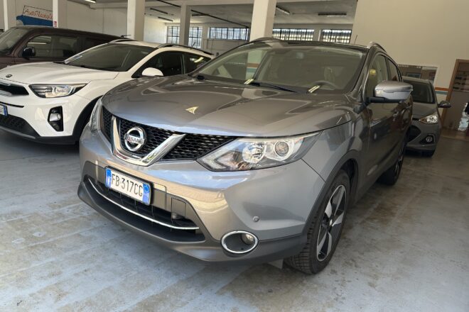 Gray Nissan SUV in a car showroom, with a white SUV beside it and other vehicles in the background.