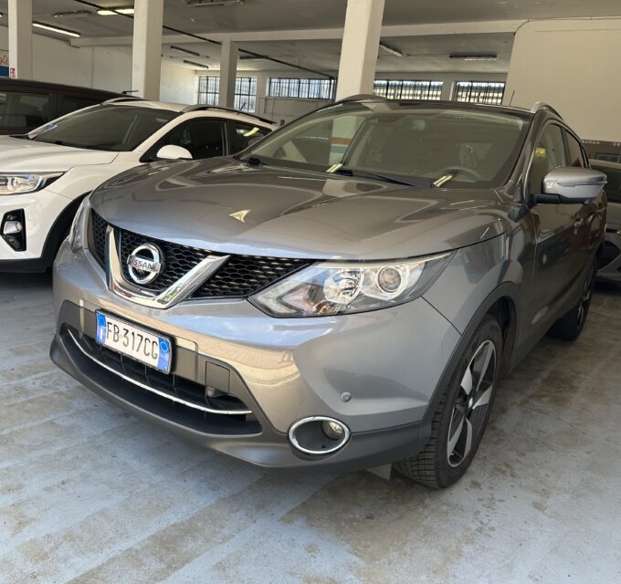 Gray Nissan SUV in a car showroom, with a white SUV beside it and other vehicles in the background.