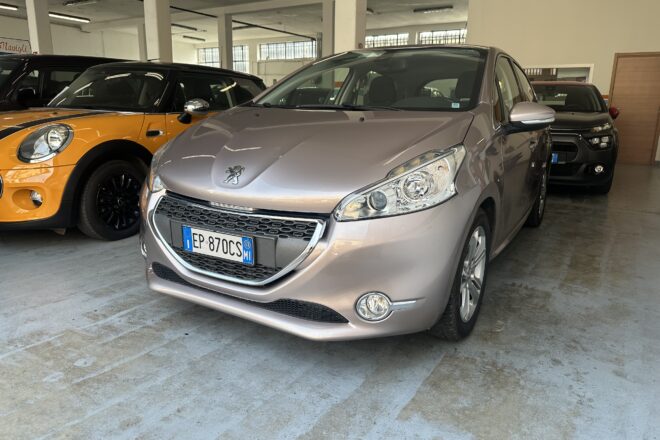 Interior of a car showroom/garage with a silver Peugeot in the foreground and an orange Mini to its left. Other vehicles visible in the background.