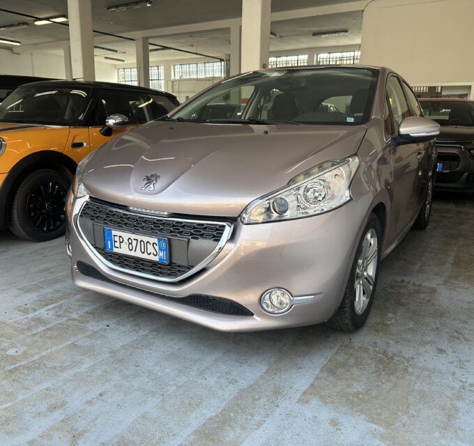 Interior of a car showroom/garage with a silver Peugeot in the foreground and an orange Mini to its left. Other vehicles visible in the background.