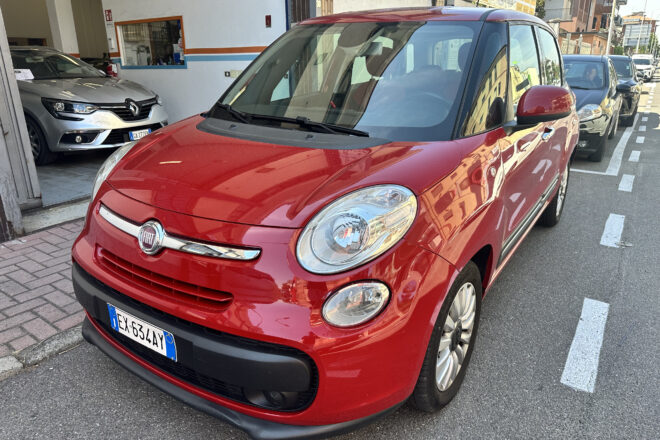 Red Fiat car in the foreground parked on a city street, with other vehicles and buildings in the background.