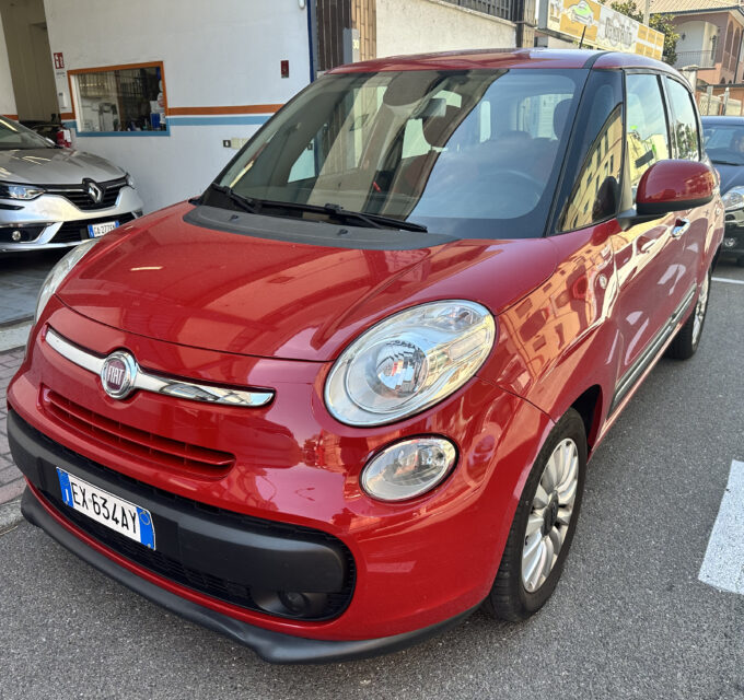 Red Fiat car in the foreground parked on a city street, with other vehicles and buildings in the background.