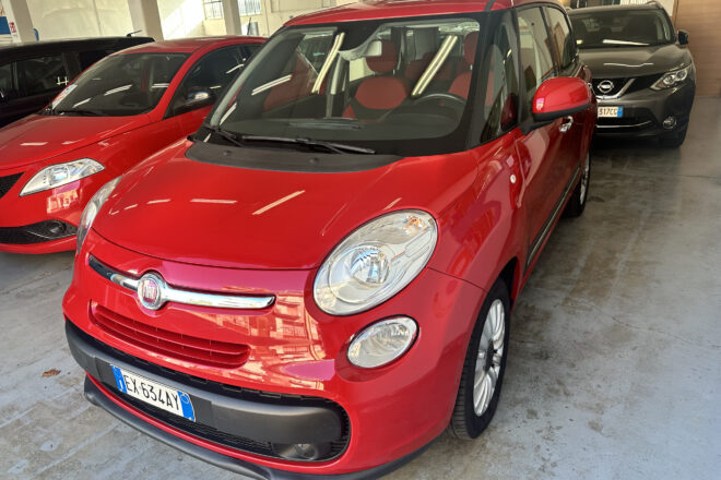 Red Fiat SUV parked indoors in a showroom, angled toward the camera with other cars in the background.