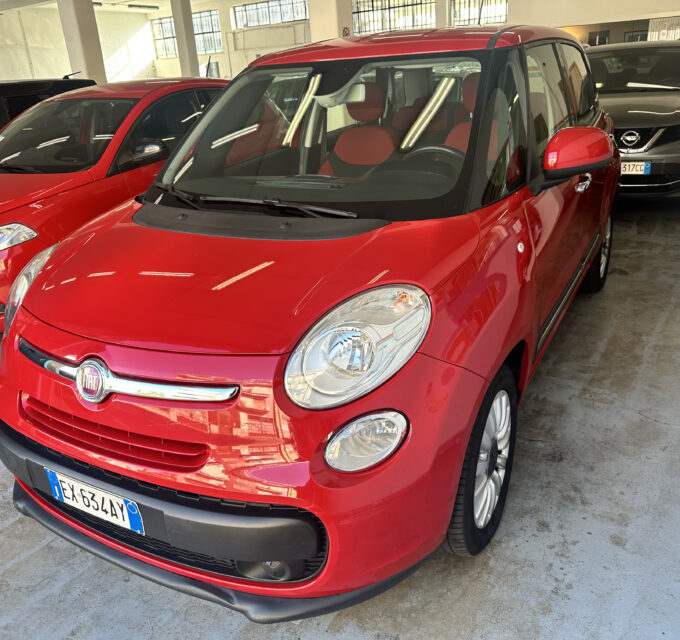 Red Fiat SUV parked indoors in a showroom, angled toward the camera with other cars in the background.