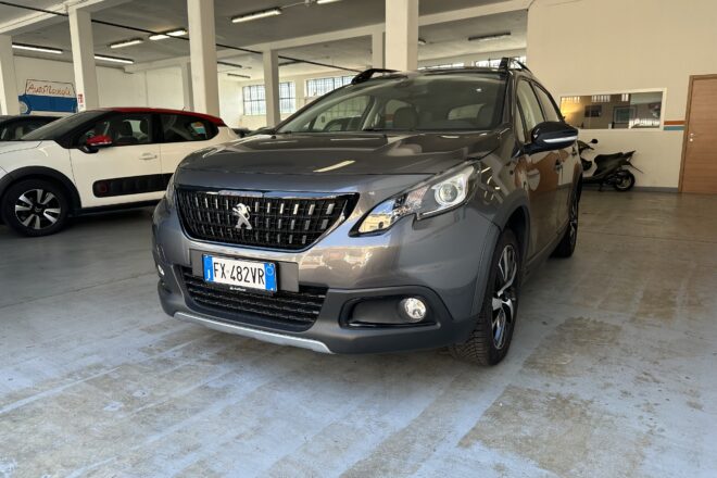 Indoor car showroom with a gray Peugeot SUV in the foreground and a white and red compact car to the left; showroom sign 'AutoNavigi' in the background.