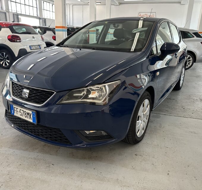 Front three-quarter view of a dark blue car in a bright indoor dealership with other cars parked nearby (license plate FF-578MK).