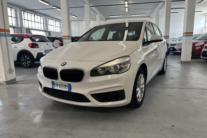 White BMW sedan in a dimly lit indoor parking garage with other cars and concrete pillars nearby.