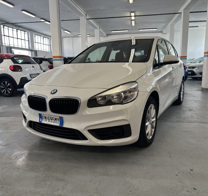 White BMW sedan in a dimly lit indoor parking garage with other cars and concrete pillars nearby.