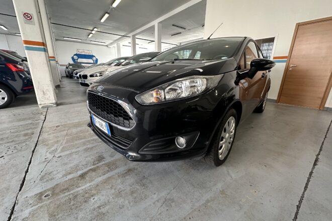 Black car parked in a dim indoor showroom with other cars lined up in the background and concrete floor.【Informative】