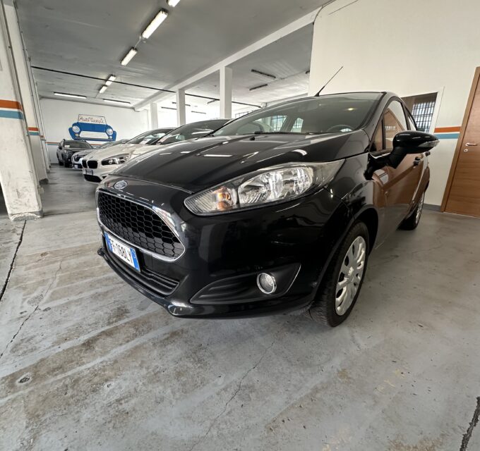 Black car parked in a dim indoor showroom with other cars lined up in the background and concrete floor.【Informative】
