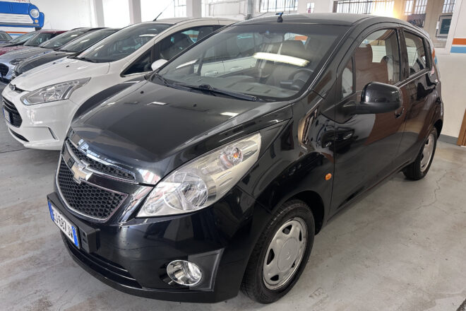 Front quarter view of a black SUV in a car dealership showroom with white and gray cars lined up in the background.