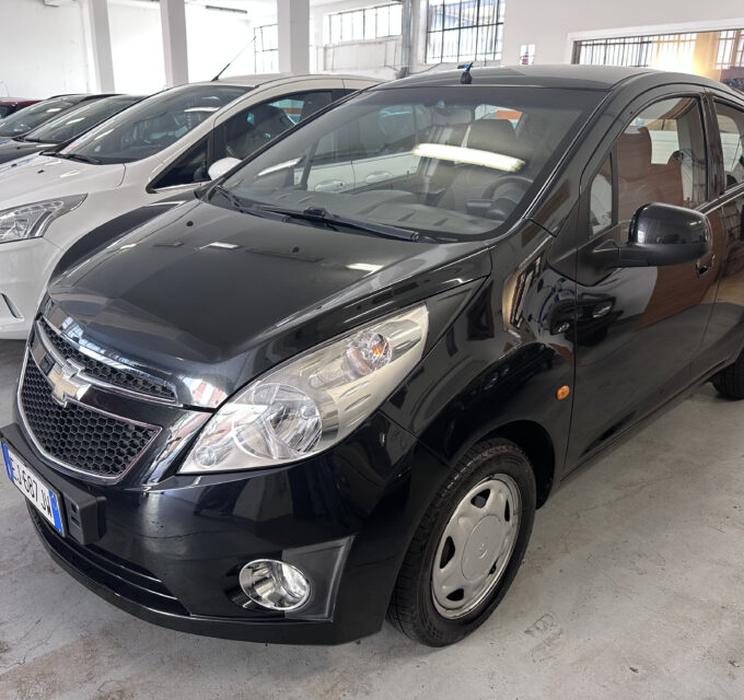 Front quarter view of a black SUV in a car dealership showroom with white and gray cars lined up in the background.