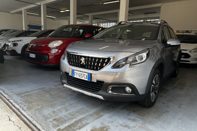 Silver Peugeot SUV in the foreground inside an indoor car showroom with other parked cars nearby.