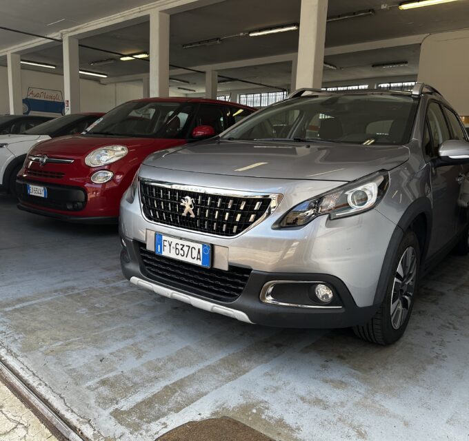 Silver Peugeot SUV in the foreground inside an indoor car showroom with other parked cars nearby.