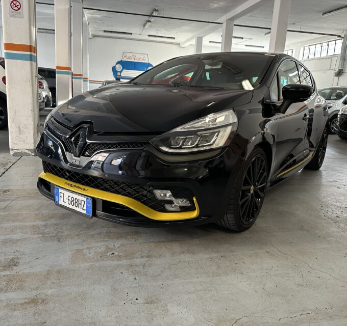 Black compact SUV with yellow front lip parked in a multi-car showroom, other vehicles visible in the background under a white ceiling with orange and blue column stripes.