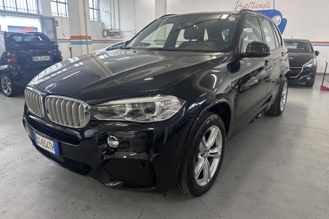 Black BMW SUV in a car showroom, with other cars visible in the background and orange-blue wall stripes in the space.