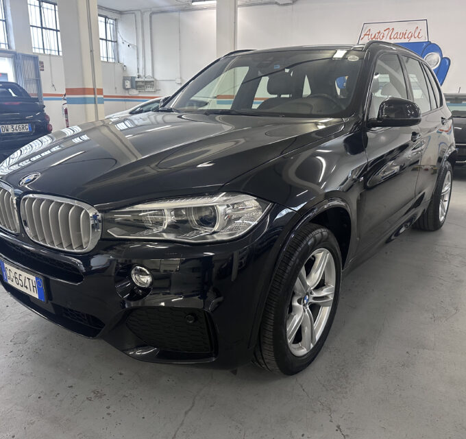 Black BMW SUV in a car showroom, with other cars visible in the background and orange-blue wall stripes in the space.