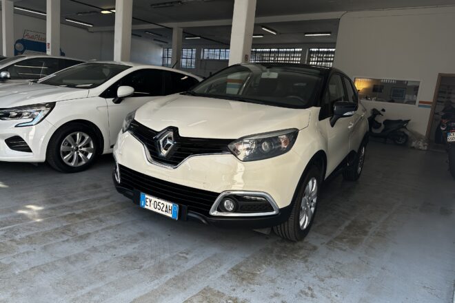 White Renault SUV parked in a showroom beside another white car, concrete floor and pillars visible in a bright indoor space