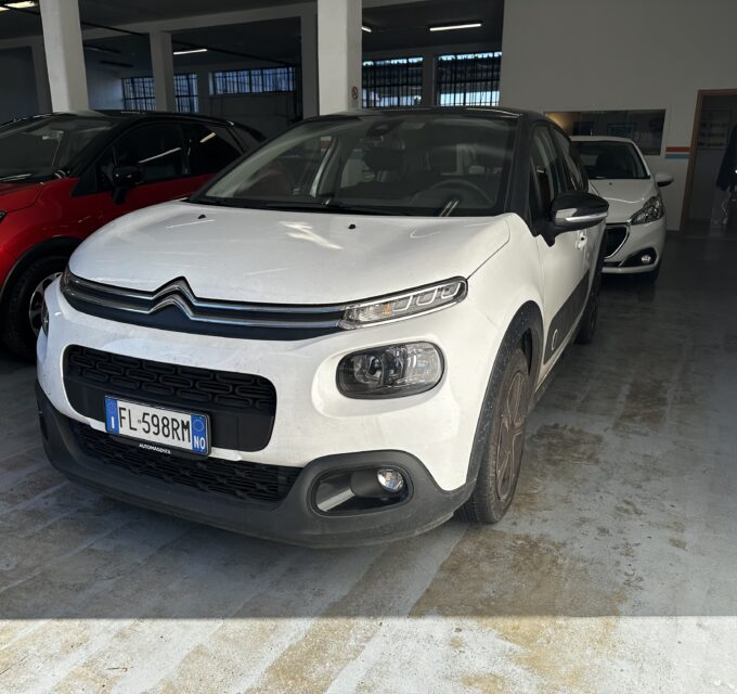 White Citroën SUV in a showroom, with a red car to the left and a white car in the background inside a dealership.