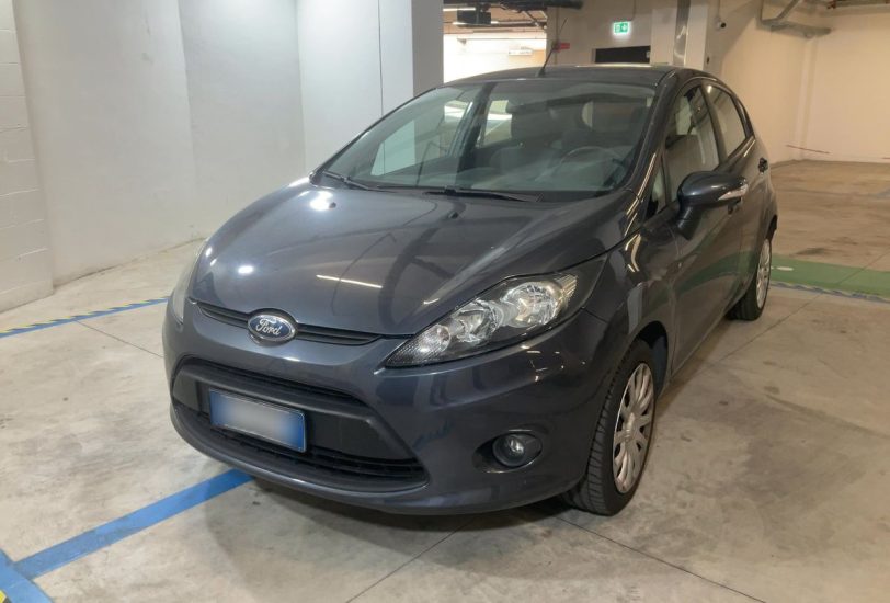 Gray Ford sedan parked in an indoor parking garage, front-left view showing headlights and grille.