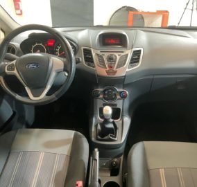 Dashboard view of a Ford interior with steering wheel, instrument cluster, center console, and manual gear shift.