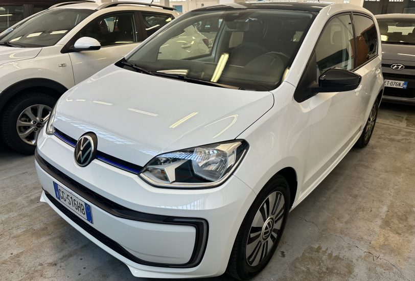 White Volkswagen hatchback parked indoors among other cars in a showroom, front angled view showing the grille and headlights.