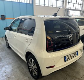 White VW minivan parked in a garage beside a white SUV, with a bright blue wall and orange stripe in the background.