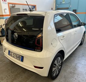 White Volkswagen car indoors in a workshop, showing the rear and passenger-side with a European license plate visible on the bumper? (rear three-quarter view)