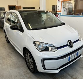 White Volkswagen car in a showroom, angled front view with other cars in the background