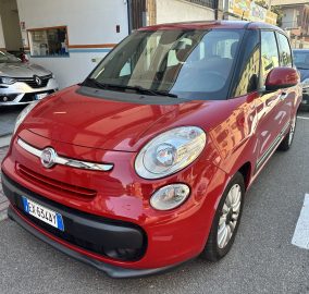 Red Fiat car in the foreground parked on a city street, with other vehicles and buildings in the background.