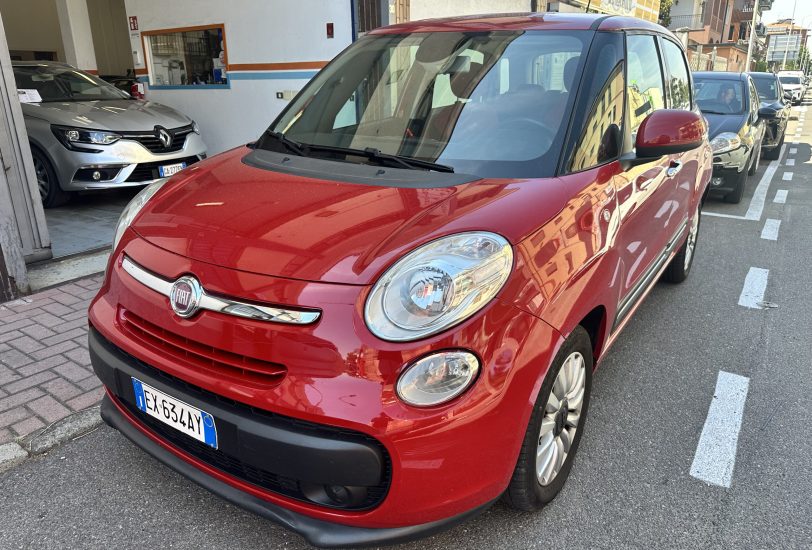 Red Fiat car in the foreground parked on a city street, with other vehicles and buildings in the background.