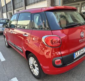 Red Fiat 500X parked in a city street lot, shown from the rear-left side with other cars and a building in the background.