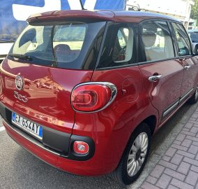 Red Fiat 500X parked on a city street, rear three-quarter view with another car beside and a blue truck in the background, license plate visible.