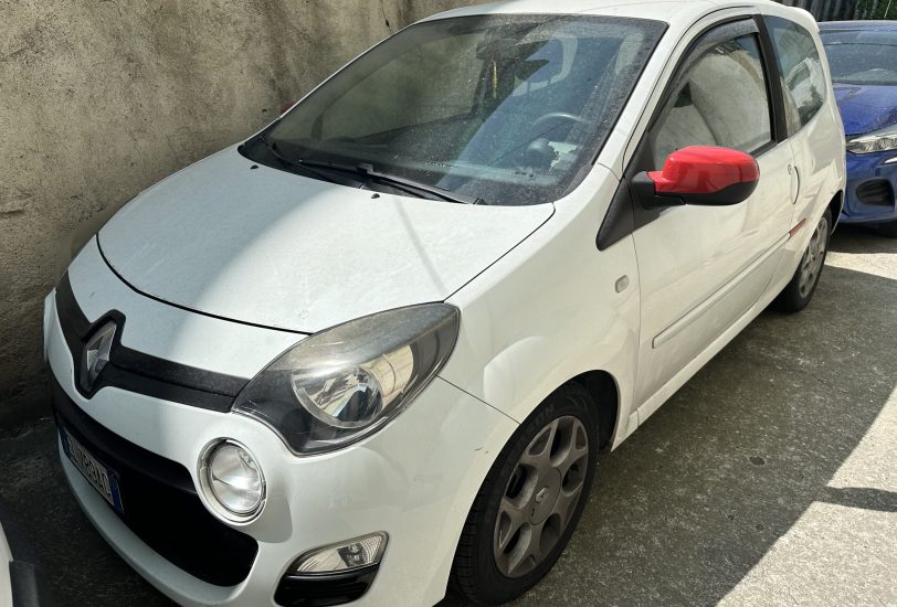 White compact car parked beside a rough concrete wall; red side mirror stands out on the driver's side.