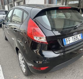 Rear view of a black Ford hatchback parked on a city street with other cars nearby, showing red taillights and rear window wiper
