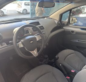 Front interior of a car showing steering wheel, dashboard, and gear shift with black fabric seats.