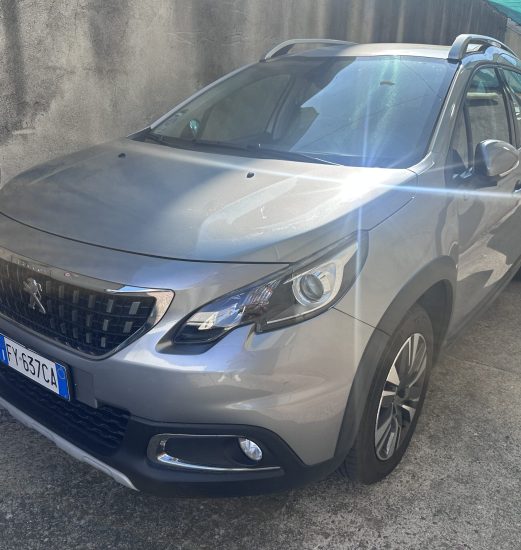 Front-right angle of a silver SUV parked in a narrow lot beside a concrete wall, with sun glare across the windshield and hood.