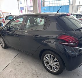 Side view of a dark gray hatchback inside a car showroom, with another car visible in the background and blue industrial doors behind.