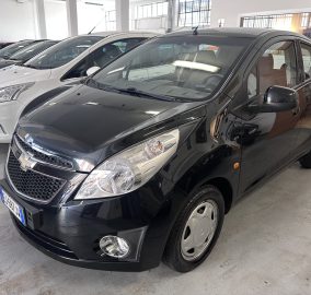 Front quarter view of a black SUV in a car dealership showroom with white and gray cars lined up in the background.