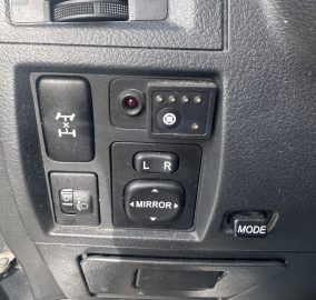 Driver-side control panel showing mirror adjustment joystick (L/R) and a mode button on textured black dash surface.