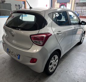 Silver Hyundai hatchback photographed from the rear driver's side, parked inside a light-colored garage with a European license plate visible.