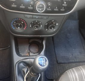 Center console with a manual gear shift knob showing N, R, + and - beside climate and media controls in a dusty car interior.