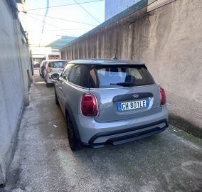 Narrow alley with tall concrete walls and multiple parked cars, including a gray Mini at the foreground.