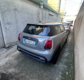 Grey Mini Cooper parked in a narrow concrete alley between tall walls, license plate GH-801LE visible on the rear.