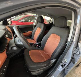 Front interior of a car showing black and orange seat upholstery, steering wheel, and dashboard.