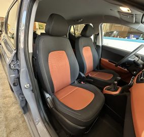 Interior of a car with black and orange seats, open driver’s door, showing steering wheel and center console.