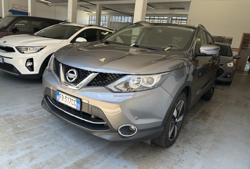 Gray Nissan SUV in a car showroom, with a white SUV beside it and other vehicles in the background.