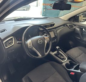 Interior view of a Nissan car: steering wheel, dashboard, center console, and front seats in black fabric.